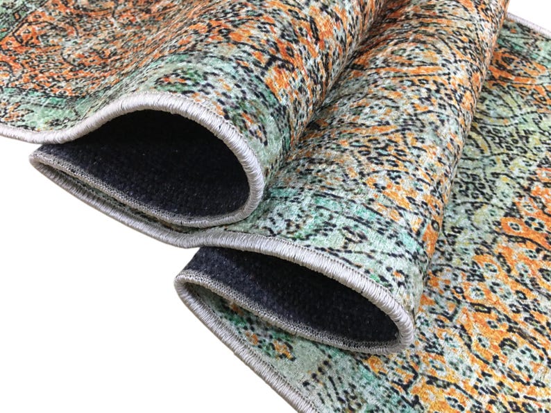 a close-up view of a colorful, patterned rug with a mix of orange, green, and black colors. The rug appears to be folded or rolled up, revealing its intricate design and texture.