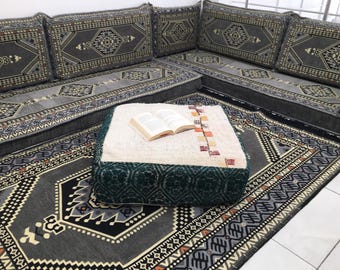 Può includere: Un cuscino da pavimento grigio e bianco con un motivo con un pouf verde e bianco con un motivo nella parte superiore. Un libro è aperto sul pouf.