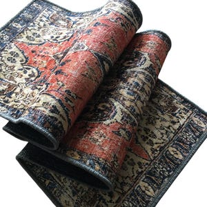 a colorful, patterned rug with a mix of red, blue, and beige colors. The rug is folded and placed on a white surface, creating a visually striking contrast.