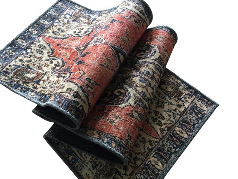 a colorful, patterned rug with a mix of red, blue, and beige colors. The rug is folded and placed on a white surface, creating a visually striking contrast.