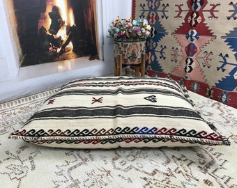 May include: A large, white and black striped floor cushion with red and blue accents. The cushion is made of woven fabric and has a geometric pattern.
