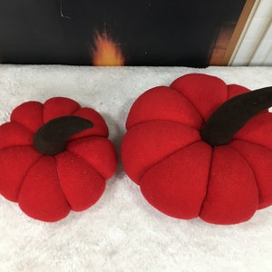 Puede incluir: Dos calabazas de fieltro rojo con tallos marrones. Las calabazas son de diferentes tamaños.