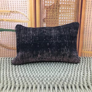 Peut inclure: Un coussin rectangulaire doté d'un textile tissé gris anthracite et noir à l'aspect vieilli et usé. Le tissu présente un motif à grain horizontal avec de subtiles variations de tons, créant un aspect texturé sur toute la surface.