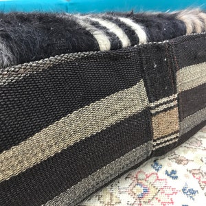 May include: A black and white striped woven cushion with a brown and beige striped panel. The cushion is made of a soft, fuzzy material.