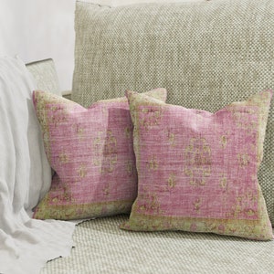 May include: Two pink and gold patterned throw pillows on a light beige couch. The pillows have a distressed, vintage look.