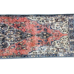 a vibrant, intricately patterned rug with a mix of red, blue, and white colors. The rug has a geometric design with floral and abstract elements, creating a visually striking and textured appearance.