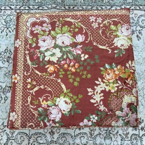 Pode incluir: Um tecido vermelho com um padr&atilde;o floral. O tecido tem uma borda amarela com um desenho repetitivo. As flores s&atilde;o em tons de rosa, branco, laranja e verde.