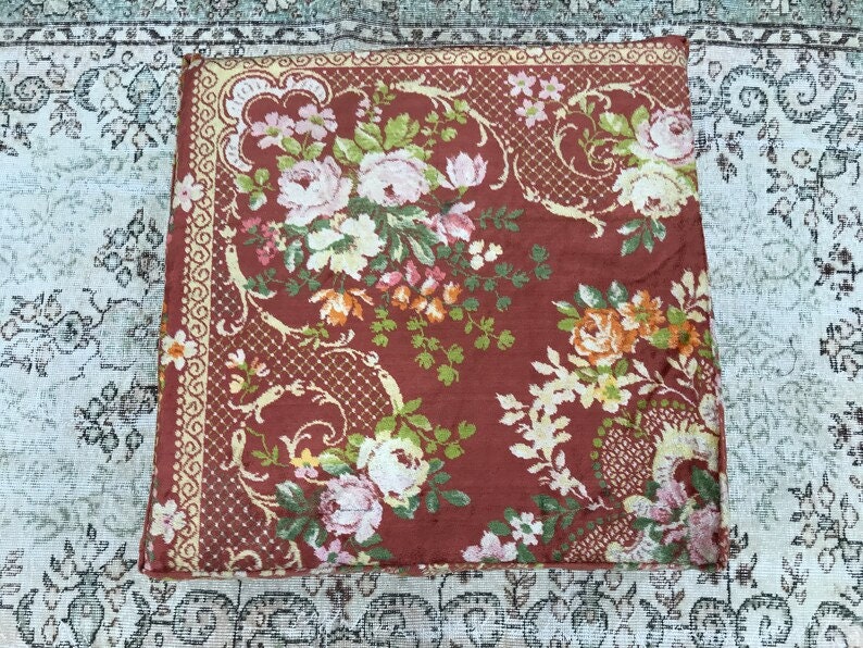 Pode incluir: Um tecido vermelho com um padr&atilde;o floral. O tecido tem uma borda amarela com um desenho repetitivo. As flores s&atilde;o em tons de rosa, branco, laranja e verde.