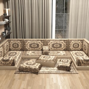 Könnte beinhalten: Ein modulares beiges Ecksofa mit gemusterten Kissen und einem passenden Teppich. Die Kissen und der Teppich weisen ein sich wiederholendes Medaillon-Design in Braun- und Beigetönen auf. Das Sofa ist in L-Form angeordnet.