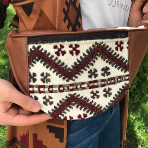 May include: A brown leather fanny pack with a white fabric front featuring a geometric pattern in shades of red, brown, and green.