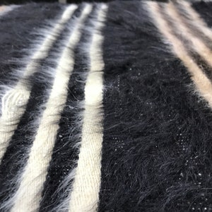 May include: Close-up of a black and white striped fuzzy fabric with a beige stripe in the background.