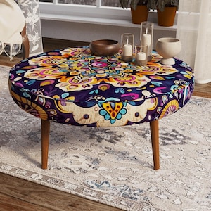 May include: A round ottoman featuring a vibrant, multi-colored mandala pattern in shades of deep purple, yellow, orange, and teal. The piece is supported by four tapered wooden legs and displays a complex, symmetrical floral-inspired design.
