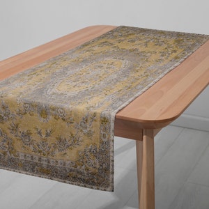 May include: A yellow and gray patterned table runner with a floral design. The runner is placed on a wooden table.