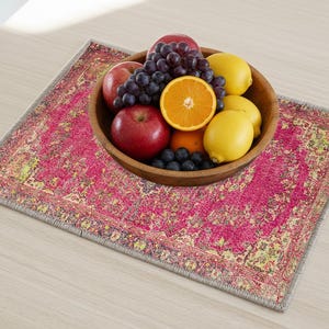 A wooden bowl filled with various fruits, including apples, oranges, and grapes, sits on a colorful rug or placemat on a wooden table.