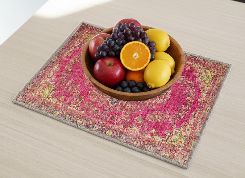 A wooden bowl filled with various fruits, including apples, oranges, and grapes, sits on a colorful rug or placemat on a wooden table.