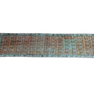 a rectangular rug with a colorful, intricate pattern in shades of green, orange, and brown.