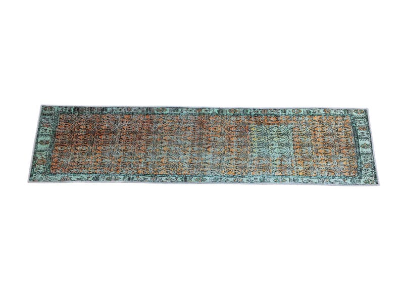 a rectangular rug with a colorful, intricate pattern in shades of green, orange, and brown.