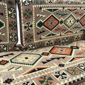 May include: A brown, beige, green, and black patterned couch cushion with a geometric design. The cushion is made of a soft, textured fabric.