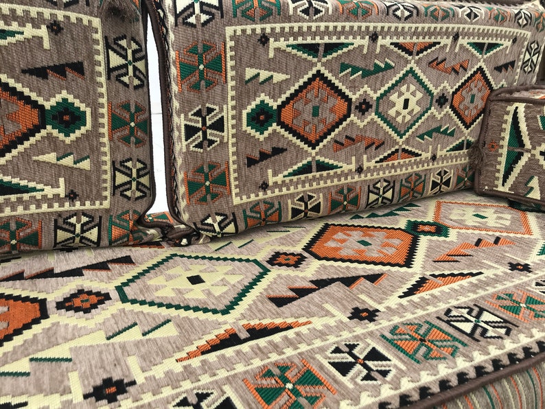 May include: A brown, beige, green, and black patterned couch cushion with a geometric design. The cushion is made of a soft, textured fabric.
