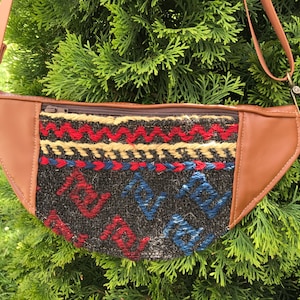 Peut inclure: Une banane en cuir marron avec un panneau avant en tissu tissé coloré. Le tissu présente un motif géométrique dans des tons de rouge, bleu, jaune et beige.