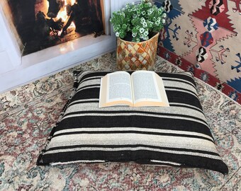 May include: A black and white striped floor cushion with a book on top. The cushion is on a patterned rug.