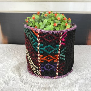 May include: A black planter with a colourful geometric pattern, filled with green plants and red flowers.