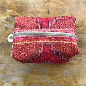 Puede incluir: Una bolsa de cremallera roja y rosa con un tirador de cremallera blanco. La bolsa tiene un diseño geométrico con una forma de diamante central.