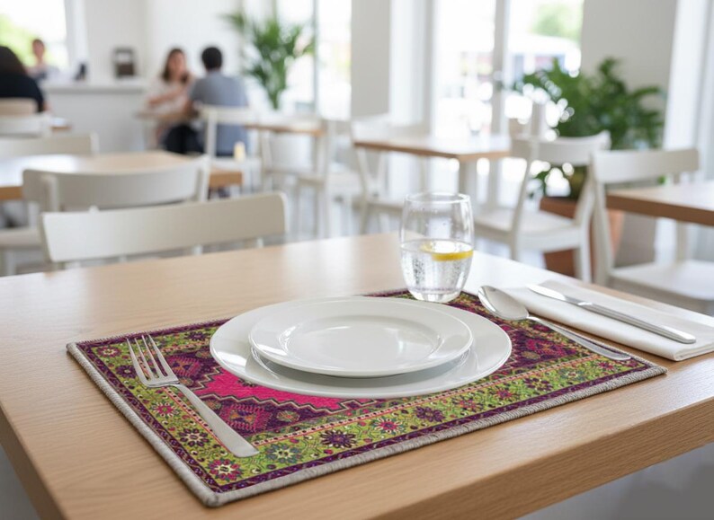 A table setting with a white plate, silverware, and a glass of water, placed on a colorful placemat in a restaurant setting.