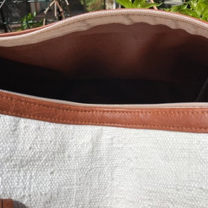 Puede incluir: El interior de una bolsa de lona blanca con un ribete de cuero marr&oacute;n alrededor de la abertura superior.