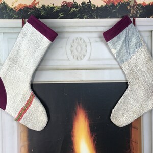 Puede incluir: Dos calcetines de Navidad blancos con ribetes burdeos y una raya roja y verde colgados de una repisa de chimenea de mármol blanco.