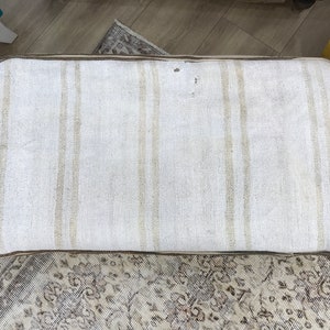 May include: A white and brown striped cushion with a brown border. The cushion is made of a woven fabric and has a slightly textured surface.