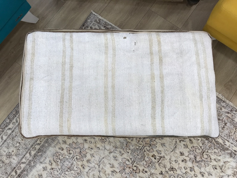 May include: A white and brown striped cushion with a brown border. The cushion is made of a woven fabric and has a slightly textured surface.
