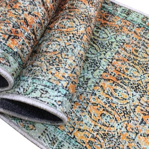 a close-up view of a colorful, patterned rug with a mix of orange, green, and black colors. The rug appears to be rolled up and placed on a surface, possibly a table or floor.
