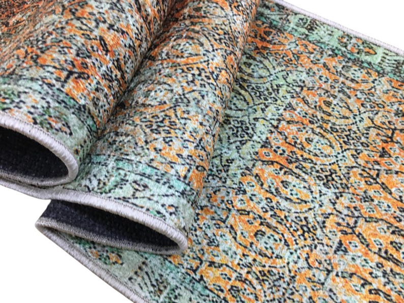 a close-up view of a colorful, patterned rug with a mix of orange, green, and black colors. The rug appears to be rolled up and placed on a surface, possibly a table or floor.