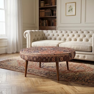 May include: A round ottoman featuring a dark, intricate, multi-colored patterned fabric with deep red, blue, and cream tones. The piece is supported by four tapered, medium-brown wooden legs, providing a stable base for the circular seat.