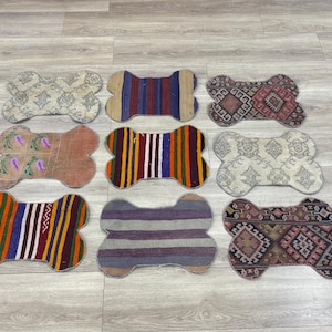 Handmade colorful Turkish Kilim pet mats, boho upcycled rug designed for pets, unique bone-shaped feeding mat, durable woven fabric, eco-friendly recycled carpet, decorative home accent, vibrant patterns and textures, comfortable and easy-to-clean, perfect for indoor or outdoor use, adds charm to any pet feeding area, ideal gift for pet lovers, artisanal inspired Turkish weave, stylish addition to pet space, one-of-a-kind handmade design.