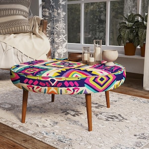 May include: A round ottoman featuring a vibrant, multi-colored geometric pattern in shades of pink, yellow, blue, and orange. The piece is supported by four tapered wooden legs and includes a cushioned top surface with a matching fabric design.