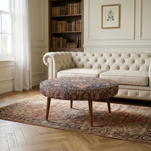 May include: A round ottoman featuring a dark blue and rust-colored intricate patterned fabric upholstery. The piece is supported by four tapered wooden legs in a medium brown finish, providing a stable base for this low-profile furniture item.