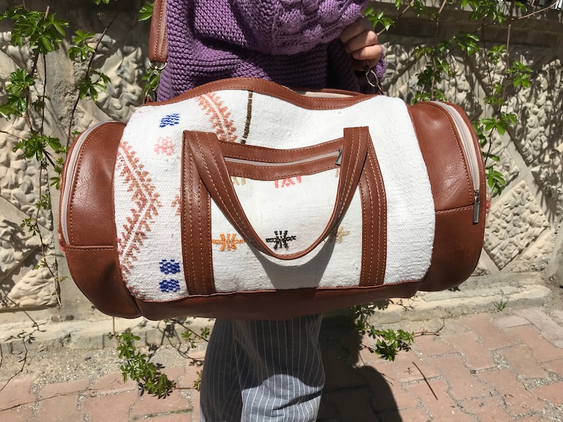 Puede incluir: Bolsa de viaje de lona blanca y marr&oacute;n con patrones geom&eacute;tricos bordados. La bolsa tiene cierre de cremallera y un asa superior.