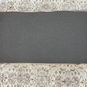 May include: A grey rectangular cushion with a dark grey fabric cover. The cushion is sitting on a patterned rug.