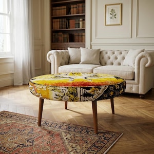 May include: A round ottoman featuring a vibrant, multi-colored fabric upholstery with intricate yellow, orange, and black patterns. The piece is supported by four tapered wooden legs and has a low-profile, circular design.
