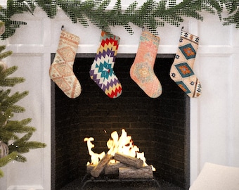 Puede incluir: Cuatro calcetines navideños con diseños estampados cuelgan sobre una chimenea con fuego encendido. Los calcetines tienen varios colores, incluyendo beige, rojo, azul y naranja. Un árbol de Navidad es visible a la izquierda.