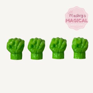 May include: Four green Hulk fist figurines. The fists are closed and have a textured surface.