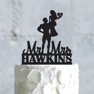 May include: Black silhouette cake topper featuring a couple, the man holding the woman in his arms. The topper says "Mr & Mrs HAWKINS" and "18.05.2020" in a heart.