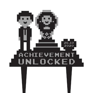 May include: Black and white pixelated cake topper with the text "ACHIEVEMENT UNLOCKED" and the date "26.10 2020". The topper features two pixelated figures and a trophy.