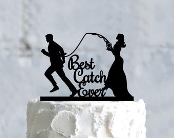 Peut inclure: Topper de gâteau en silhouette noire d'une mariée et d'un marié. Le marié tient une canne à pêche et la mariée tient une bague. Le texte "Best Catch Ever" est écrit sous le couple.