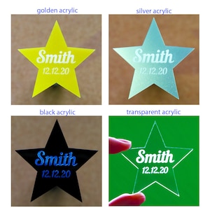 May include: Four acrylic star-shaped ornaments in gold, silver, black, and transparent. Each star has the name "Smith" and the date "12.12.20" engraved in a contrasting color. The ornaments are displayed against a neutral background.