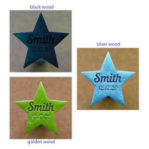 May include: Wooden star-shaped ornaments in black, silver, and golden colors. Each star has the name "Smith" and the date "12.12.20" engraved on it. The ornaments are likely for decoration or personalization.