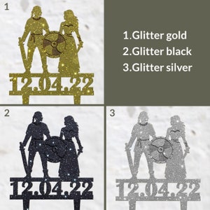 May include: Glitter cake toppers in gold, black, and silver, depicting a Viking couple with a shield and swords, and the date 12.04.22. Ideal for a wedding or anniversary celebration.