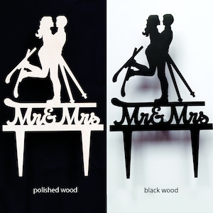 May include: Wooden wedding cake toppers in polished and black wood. The toppers feature a silhouette of a couple on skis, with the words "Mr & Mrs" below. The polished wood version is on a black background, and the black wood version is on a white background.